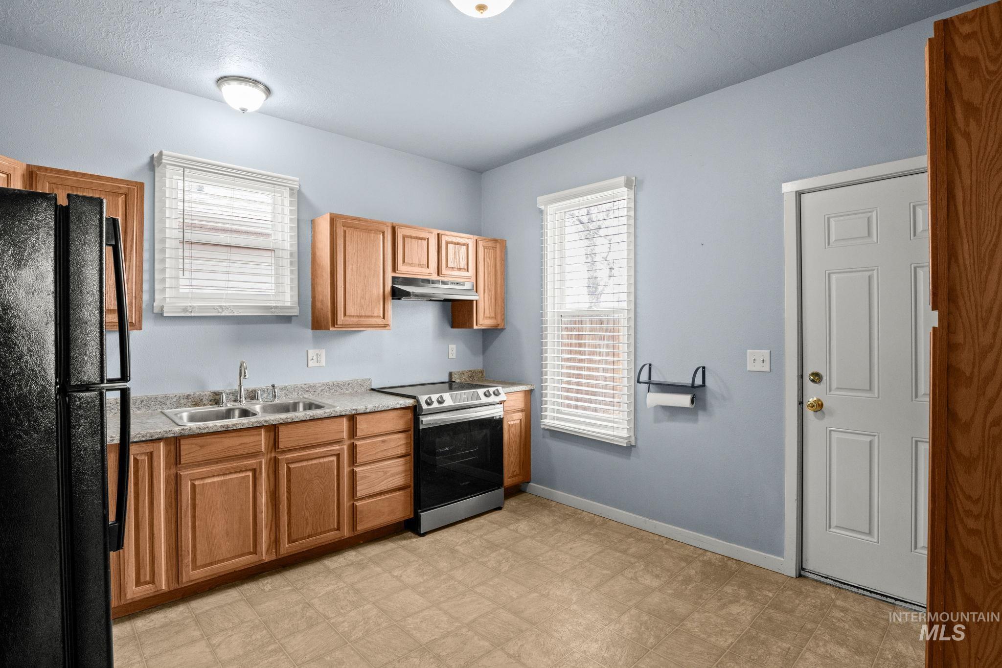 Kitchen with freestanding refrigerator, stainless steel electric range oven, a textured ceiling, brown cabinets, and light floors