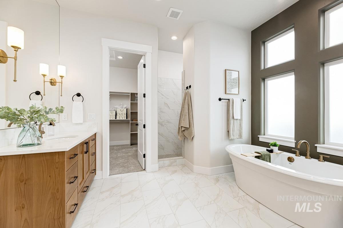 Full bath featuring a freestanding tub, vanity, a spacious closet, a tile shower, and light marble finish floors