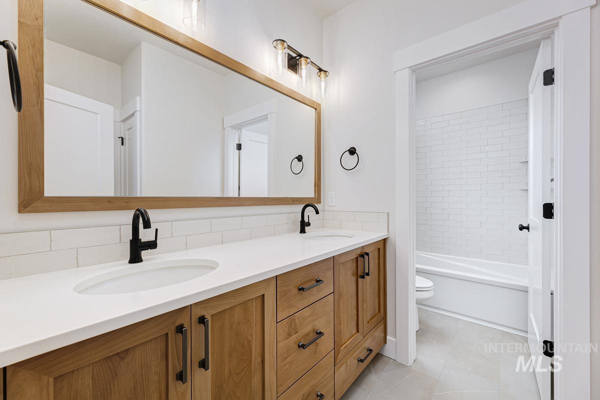 Full bathroom with double vanity, light tile patterned flooring, tub / shower combination, and tasteful backsplash
