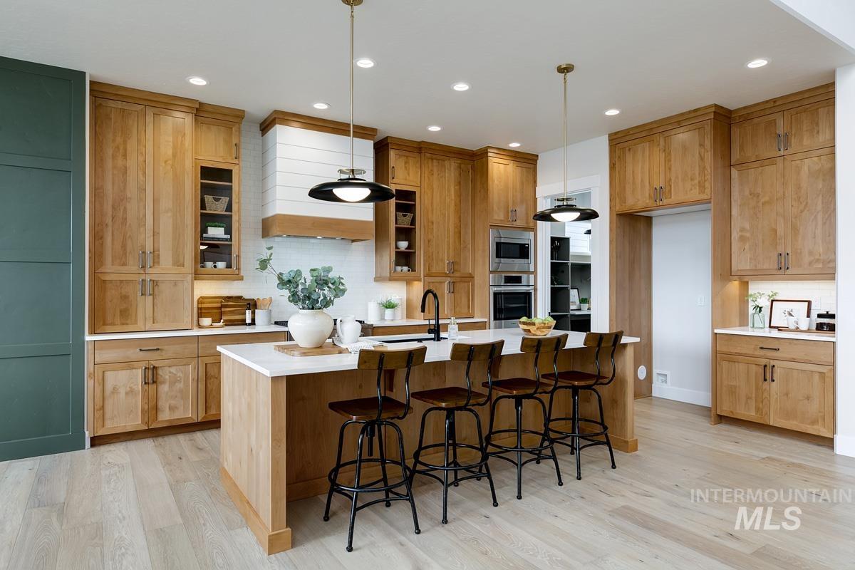 Kitchen featuring a kitchen breakfast bar, an island with sink, decorative backsplash, decorative light fixtures, and light wood finished floors