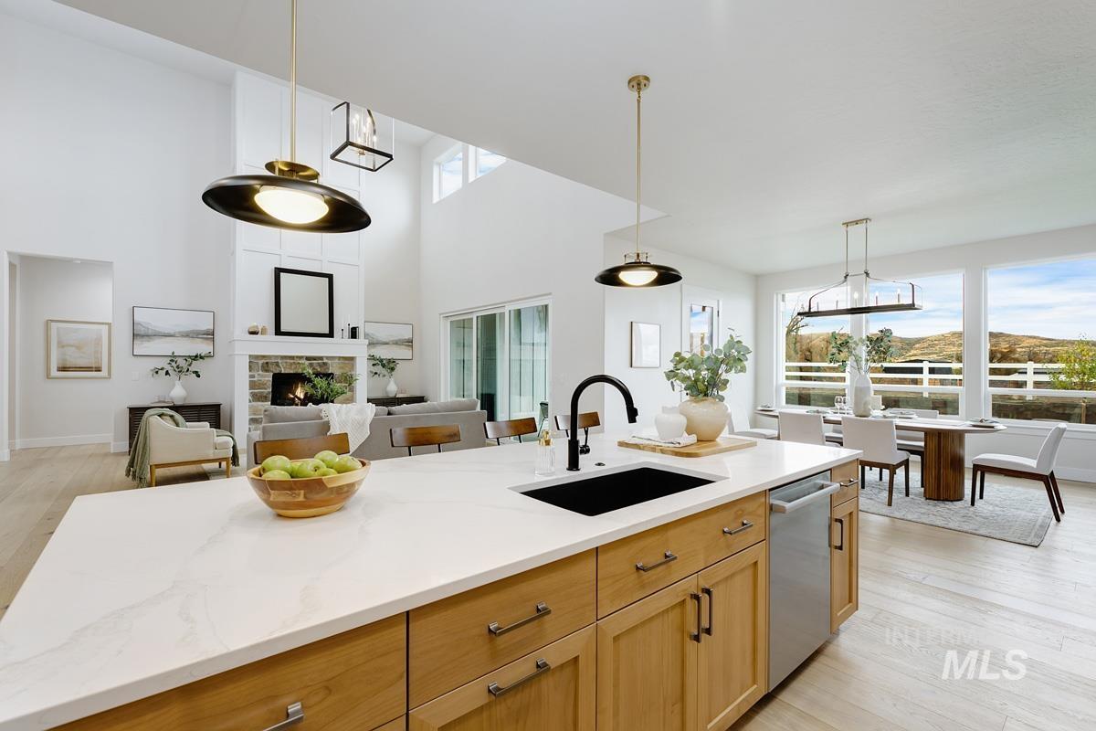 Kitchen featuring light wood finished floors, pendant lighting, a stone fireplace, open floor plan, and a towering ceiling