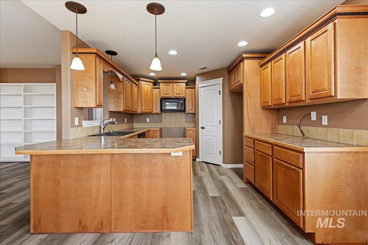 Kitchen with a peninsula, pendant lighting, light wood-style floors, black microwave, and a textured ceiling