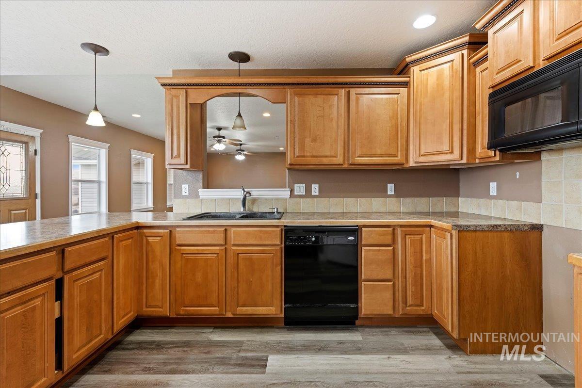 Kitchen with black appliances, decorative light fixtures, light wood-type flooring, a ceiling fan, and brown cabinetry