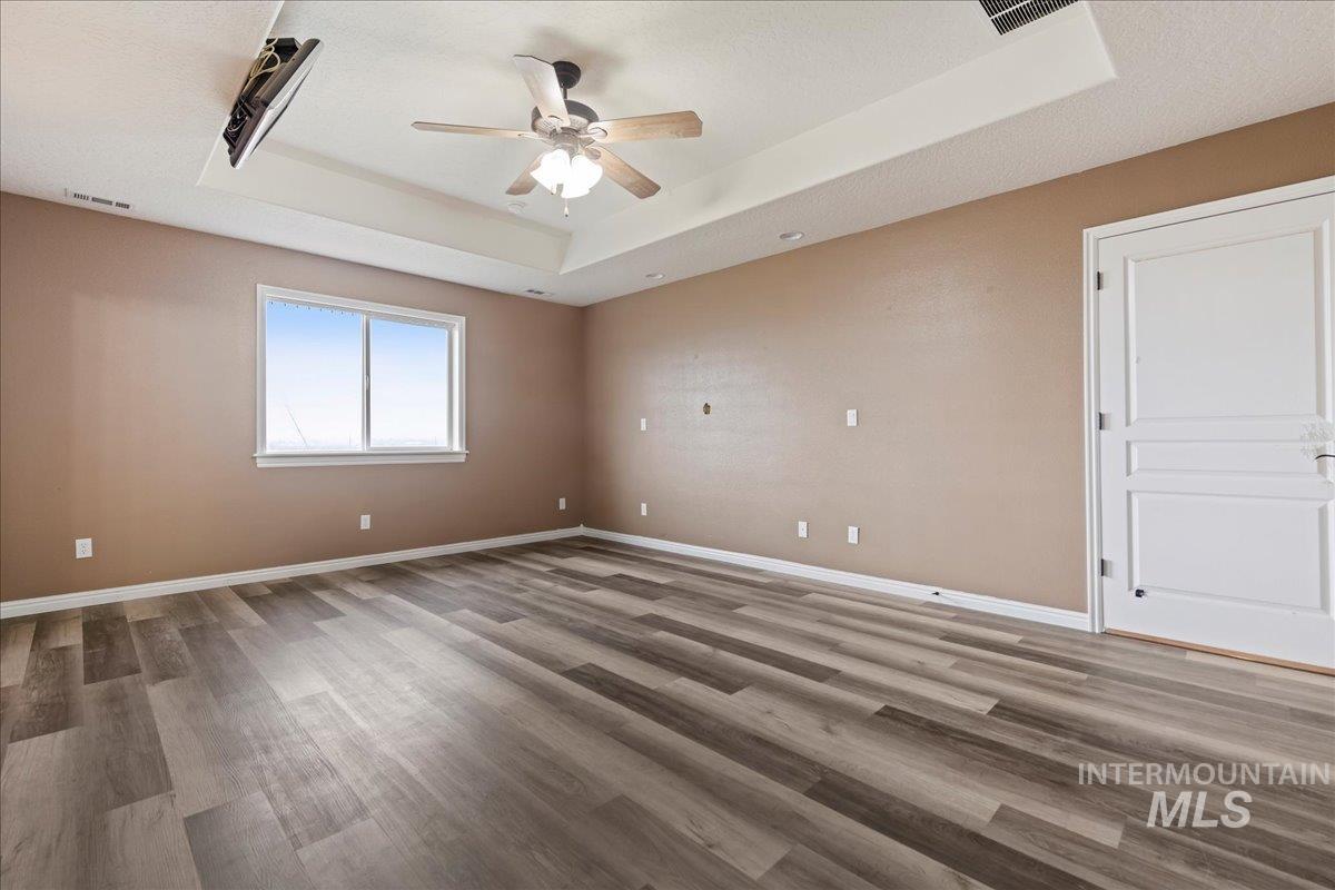 Primary bedroom with a raised ceiling, light wood-style flooring, and a ceiling fan