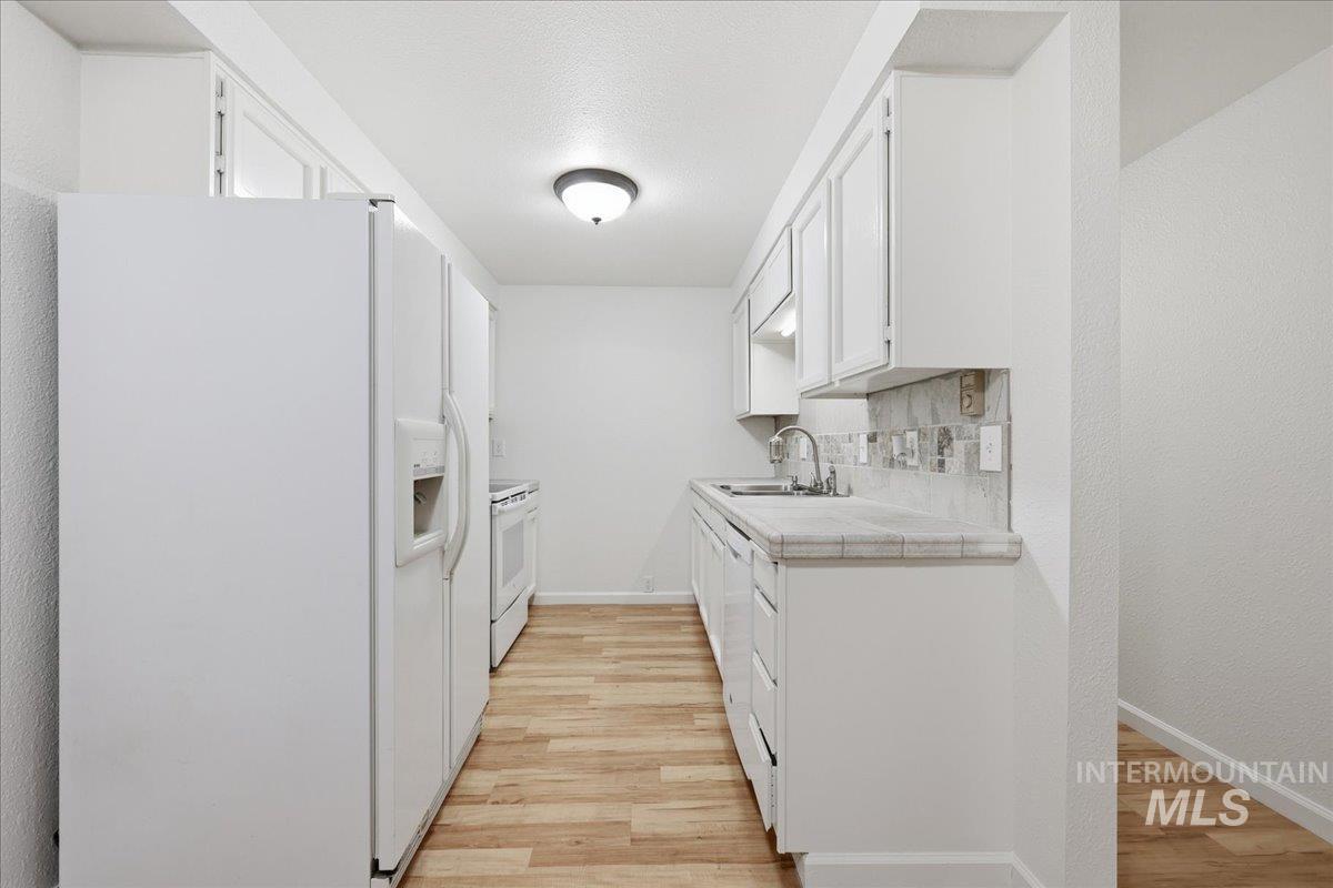 Kitchen featuring white appliances, white cabinets, light wood finished floors, tasteful backsplash, and a textured ceiling