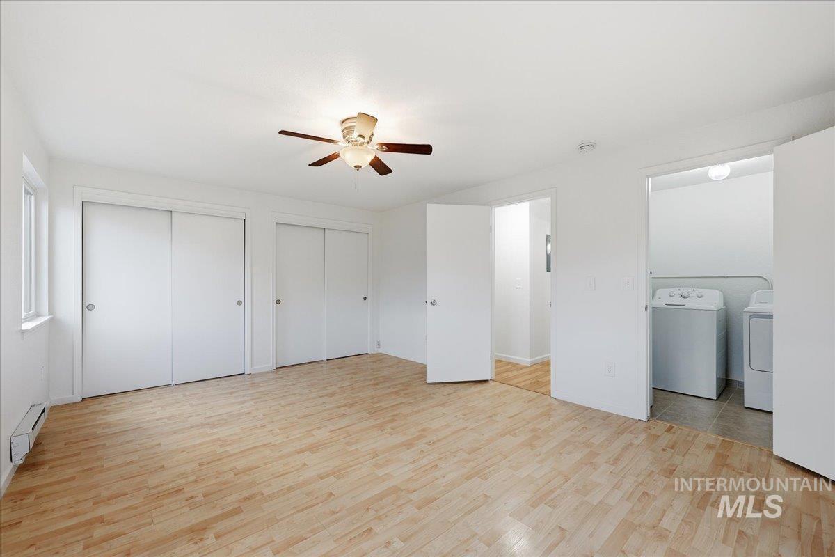 Unfurnished bedroom featuring two closets, light wood-style flooring, a ceiling fan, washing machine and clothes dryer, and baseboard heating