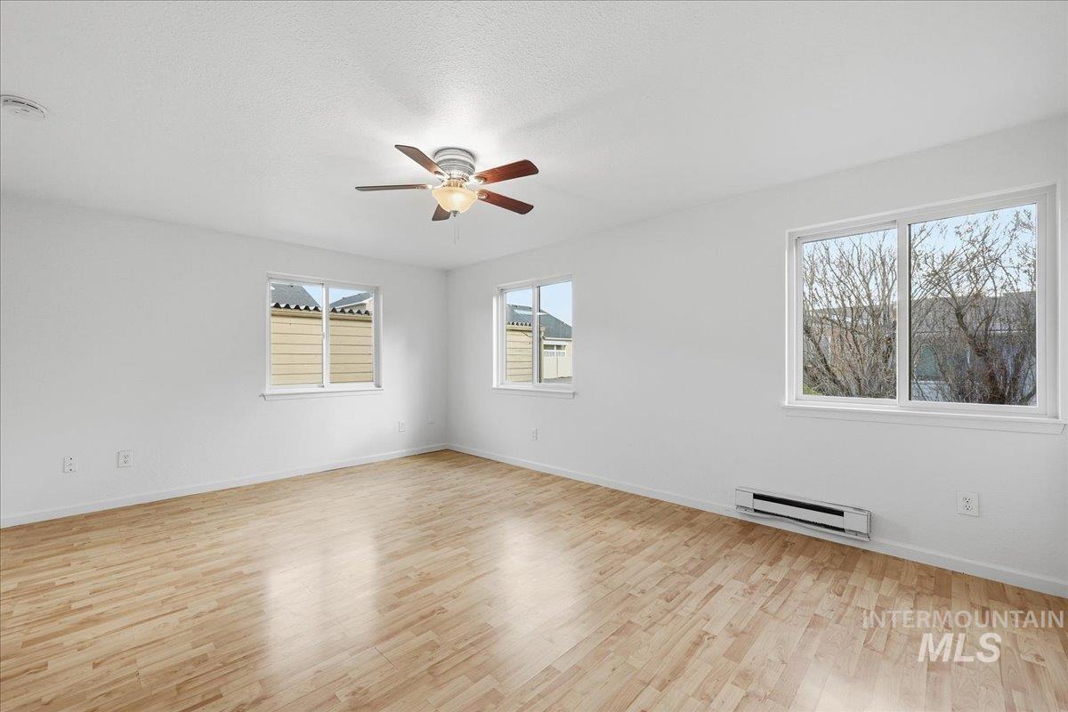 Empty room with light wood-style flooring, a baseboard radiator, a ceiling fan, and a textured ceiling