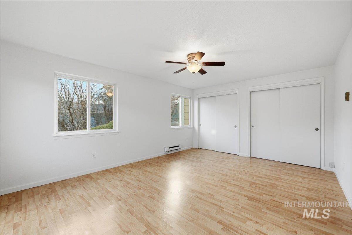 Unfurnished bedroom featuring two closets, light wood finished floors, ceiling fan, and a baseboard heating unit