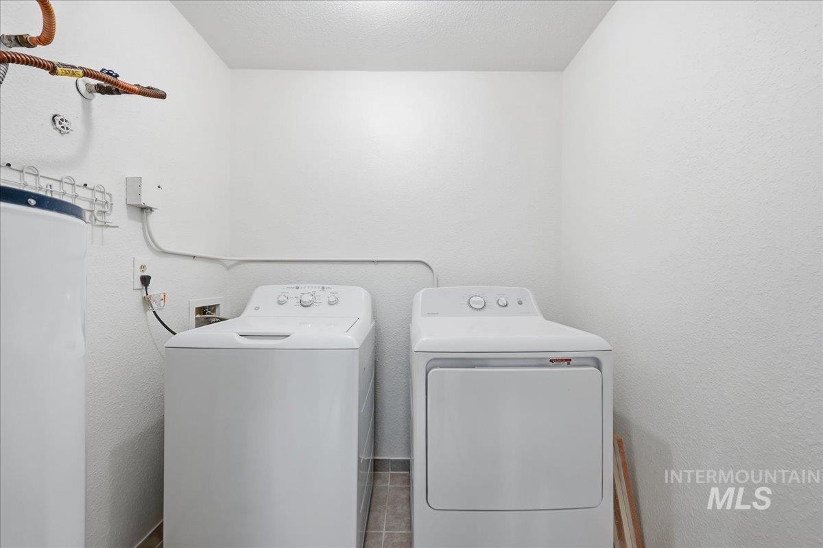 Washroom with water heater, washing machine and dryer, a textured wall, and a textured ceiling