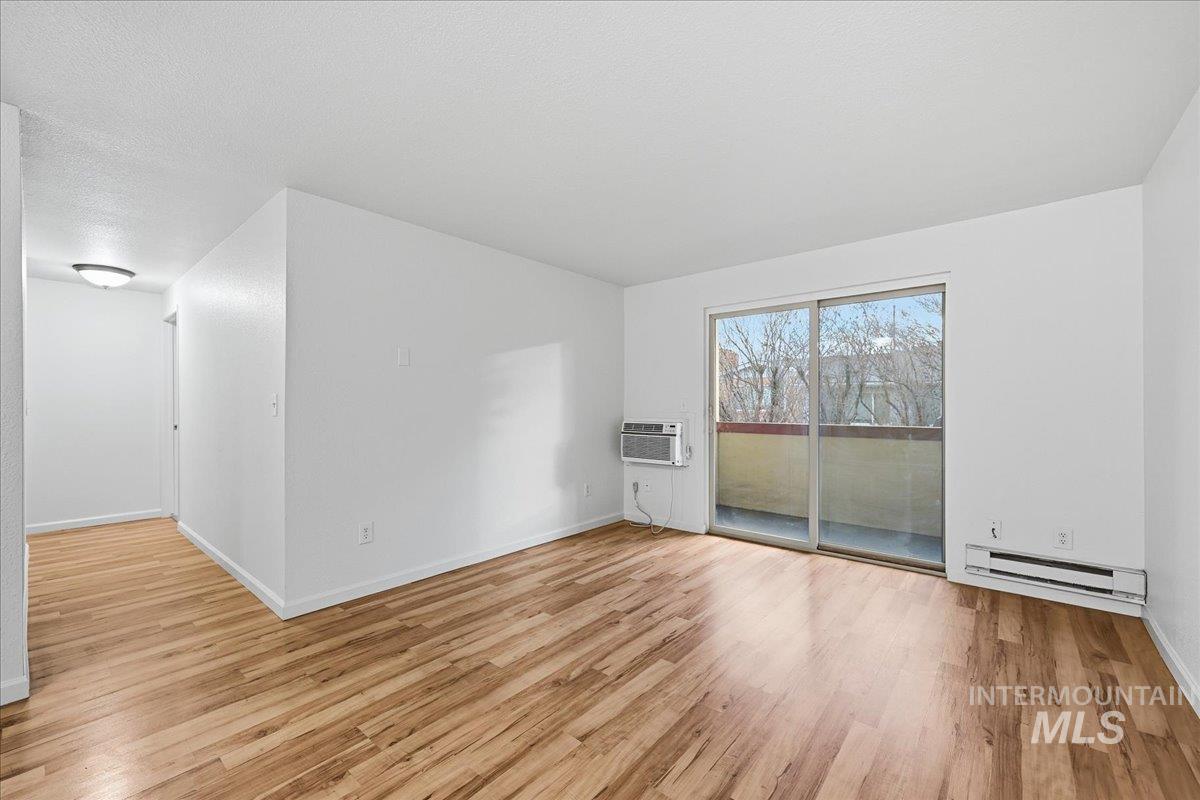 Unfurnished room with light wood-style floors, baseboard heating, a textured ceiling, and an AC wall unit