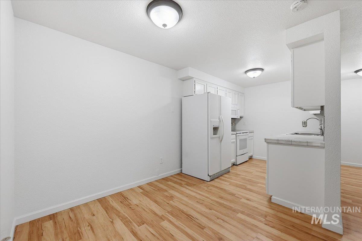 Kitchen featuring tile countertops, white appliances, white cabinets, a textured ceiling, and light wood finished floors