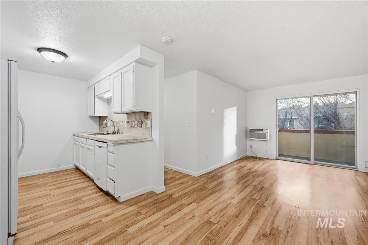 Kitchen with white cabinetry, light countertops, white appliances, light wood finished floors, and a textured ceiling