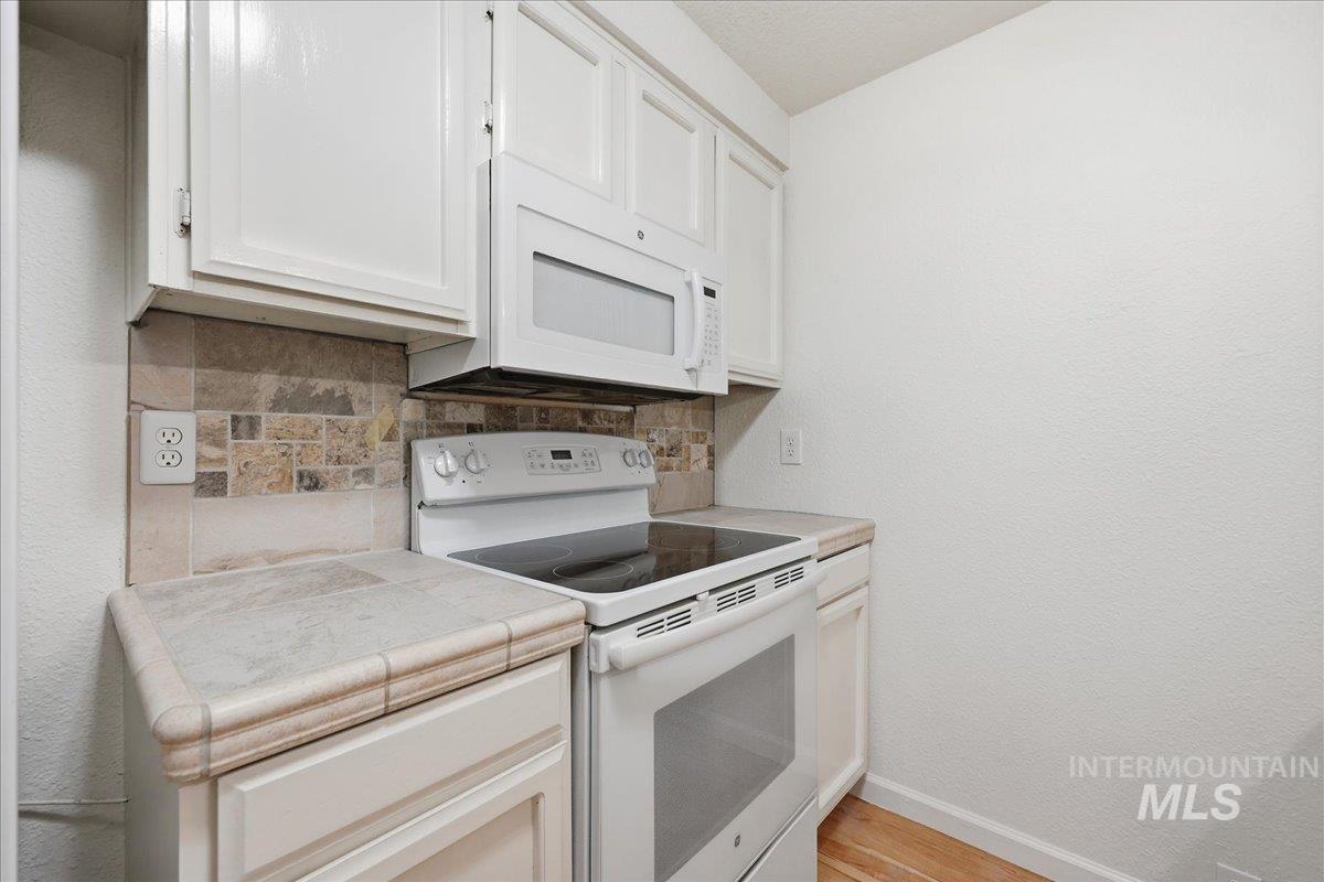 Kitchen featuring white appliances, tasteful backsplash, tile countertops, white cabinetry, and a textured wall