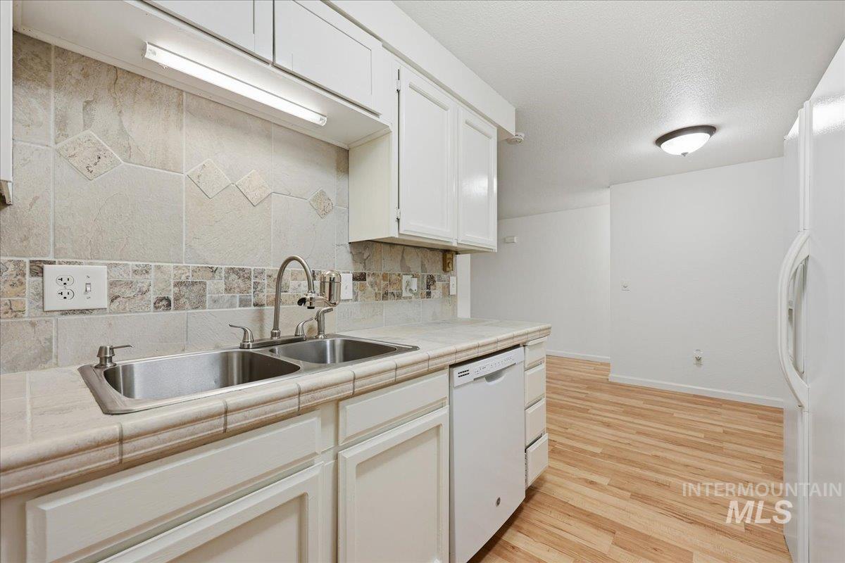 Kitchen featuring tile counters, light wood finished floors, white appliances, decorative backsplash, and a textured ceiling