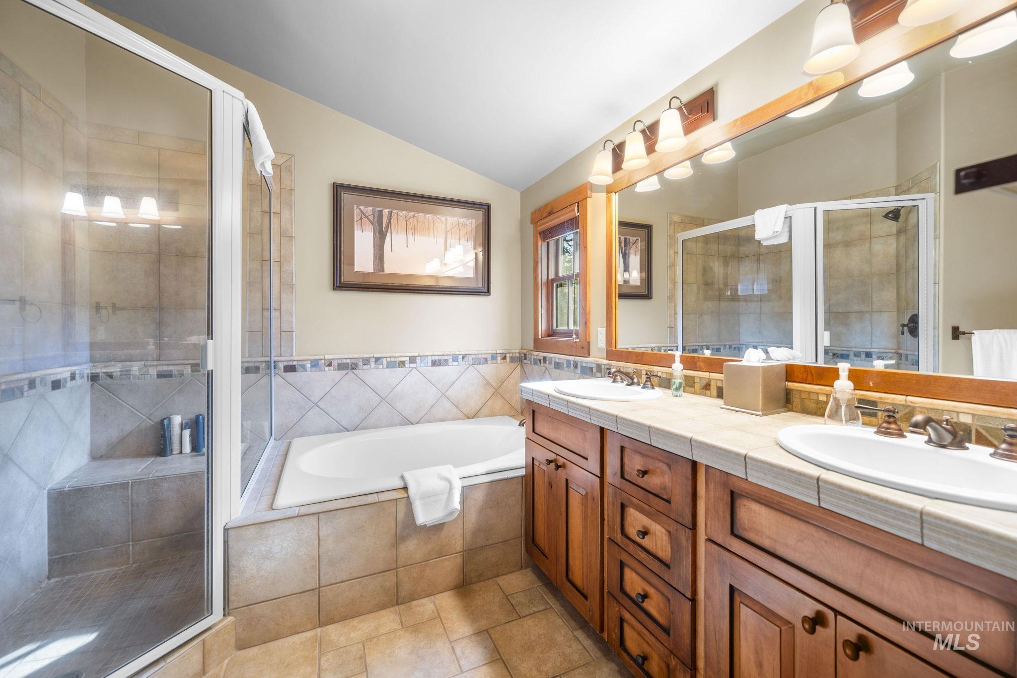 Bathroom with double vanity, a stall shower, a bath, and vaulted ceiling