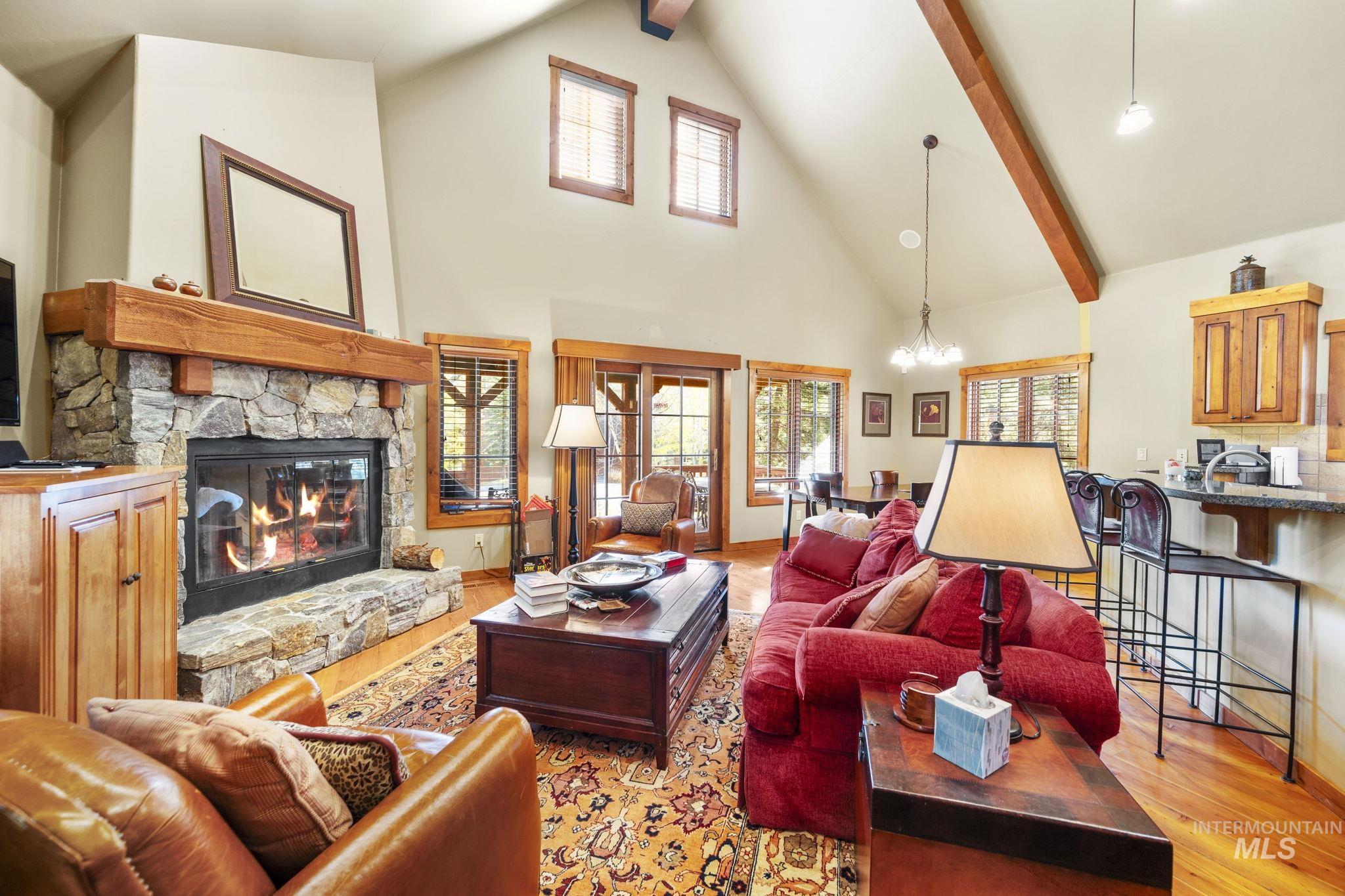 Living room featuring light wood-style flooring, a stone fireplace, high vaulted ceiling, beamed ceiling, and a chandelier