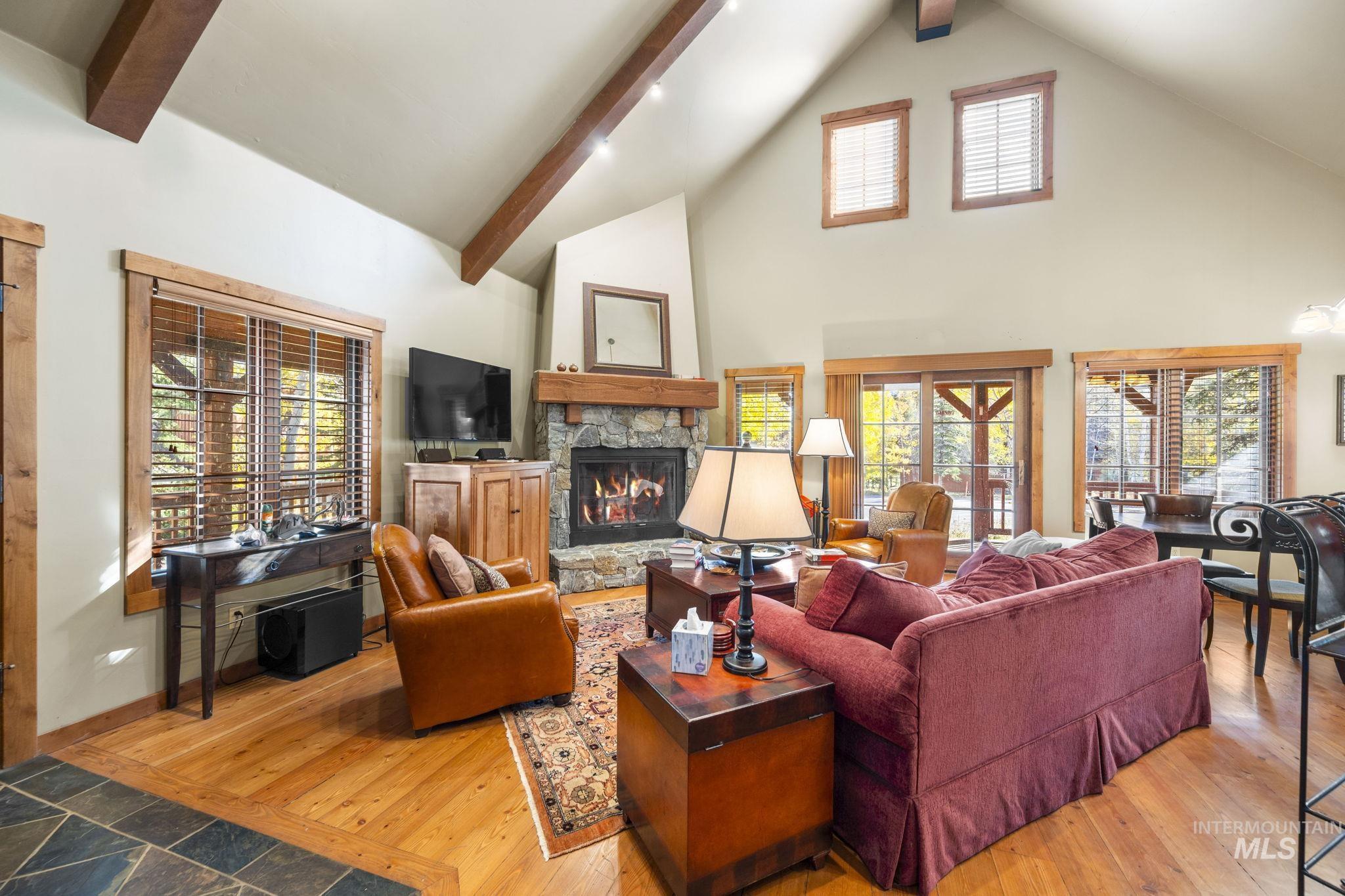 Living area featuring a stone fireplace, light wood-type flooring, high vaulted ceiling, and beam ceiling