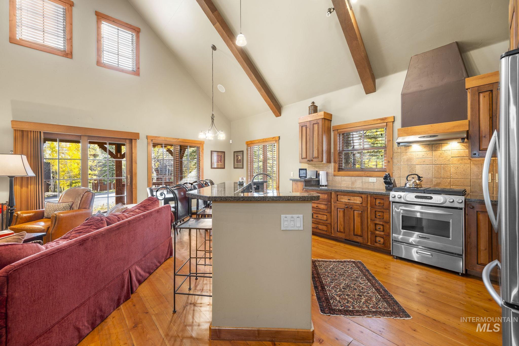Kitchen with a kitchen bar, high vaulted ceiling, stainless steel appliances, a kitchen island with sink, and brown cabinetry