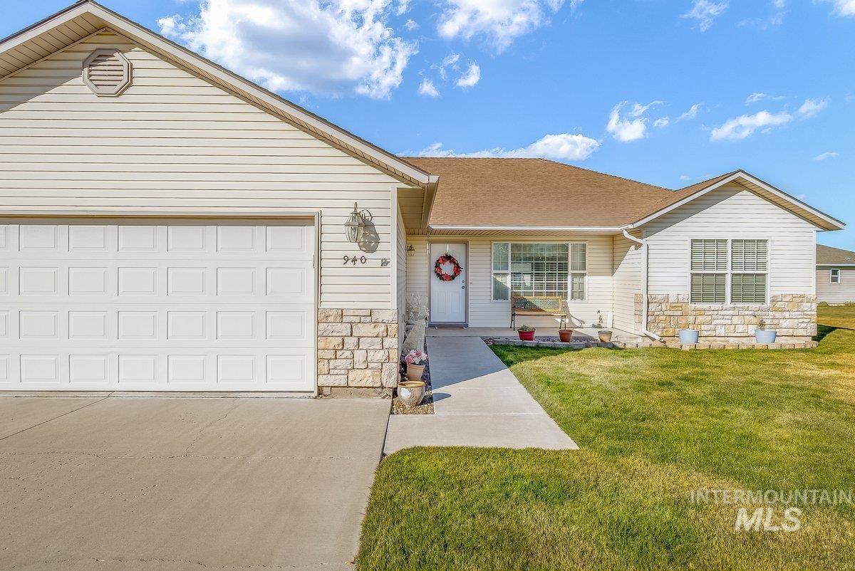 Ranch-style home with stone siding, a front yard, concrete driveway, an attached garage, and a shingled roof