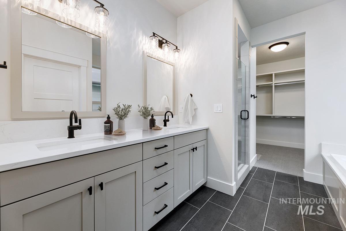 Full bath with double vanity, a spacious closet, dark tile patterned flooring, and a shower stall