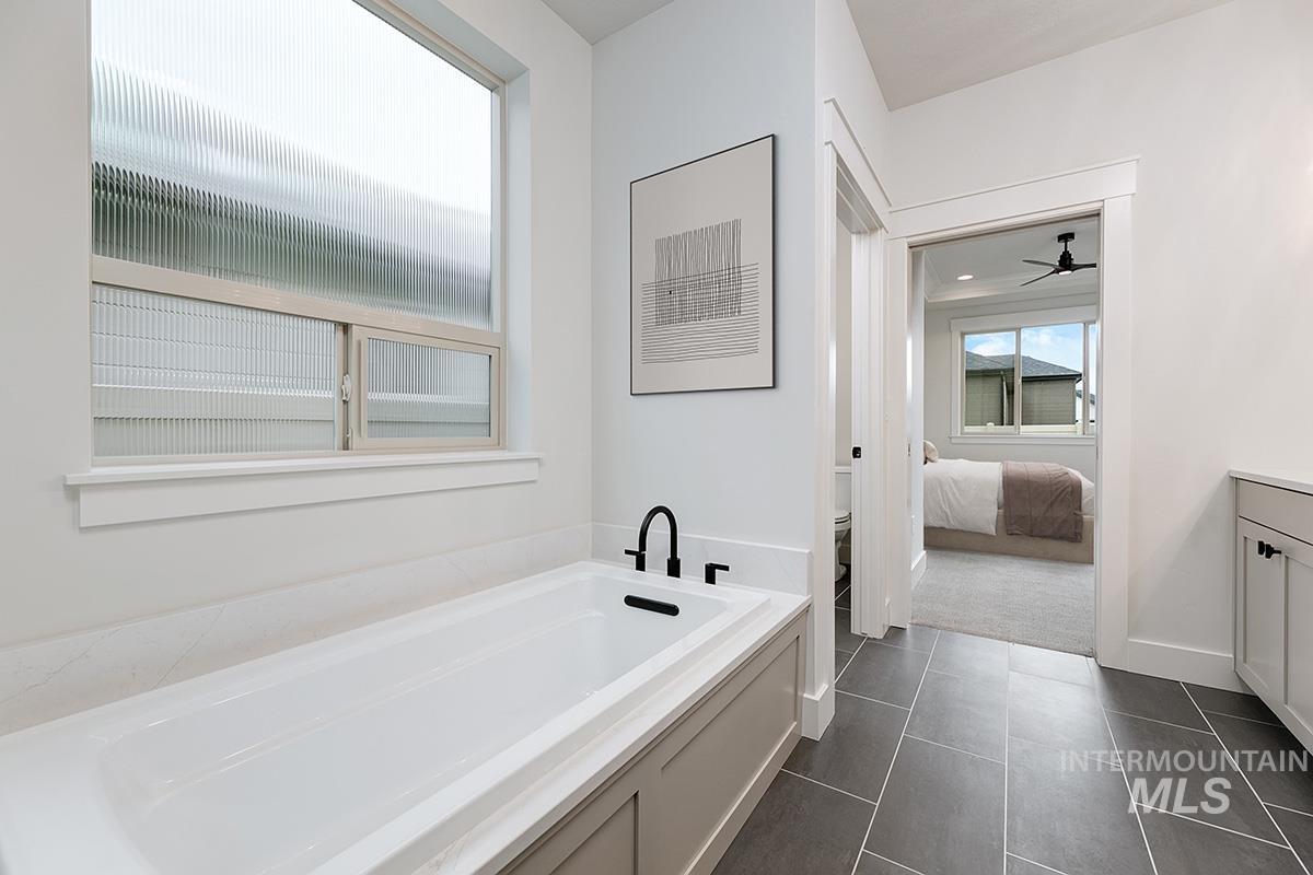 Ensuite bathroom featuring a bath, vanity, a ceiling fan, dark tile patterned floors, and dark carpet