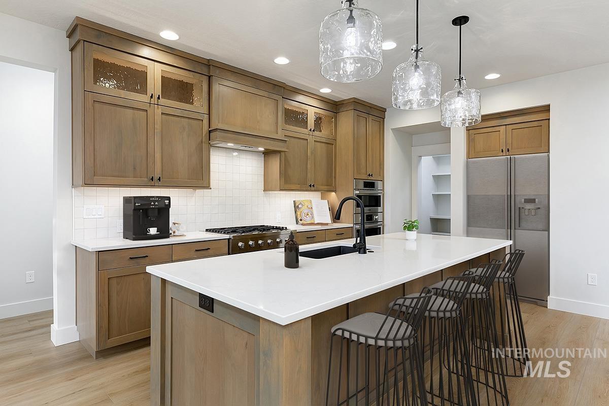 Kitchen featuring stainless steel appliances, glass insert cabinets, brown cabinetry, backsplash, and a kitchen bar