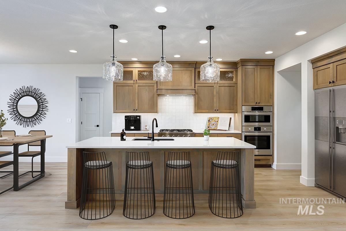 Kitchen with appliances with stainless steel finishes, a kitchen bar, tasteful backsplash, an island with sink, and hanging light fixtures