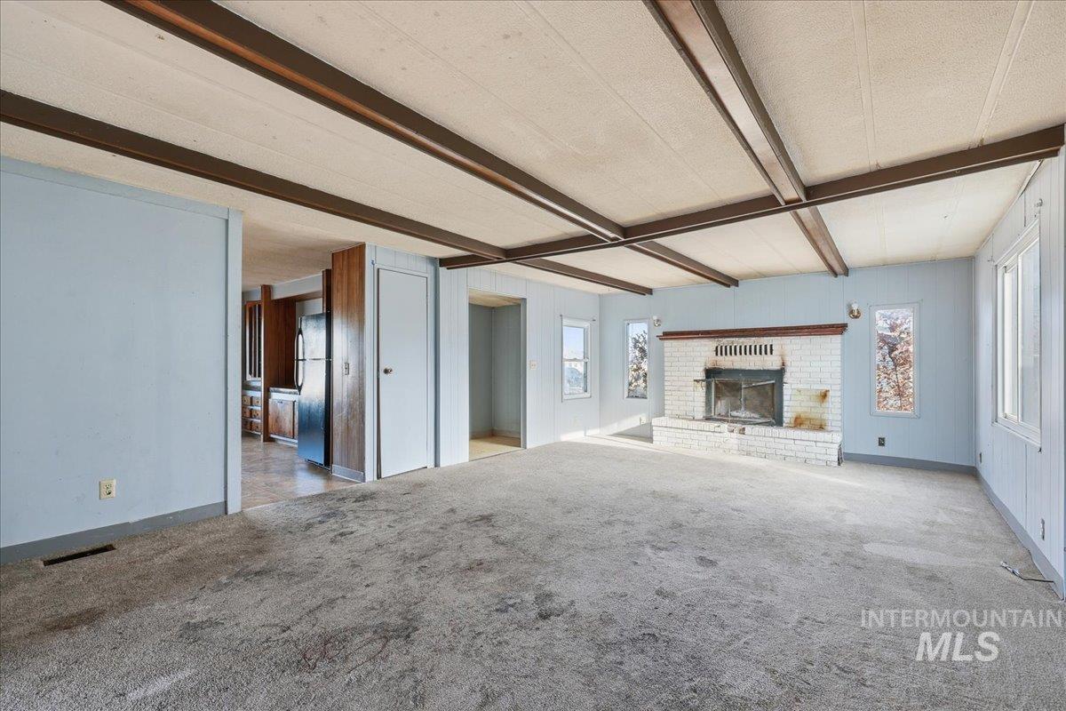 Unfurnished living room featuring beamed ceiling, a brick fireplace, carpet, and plenty of natural light