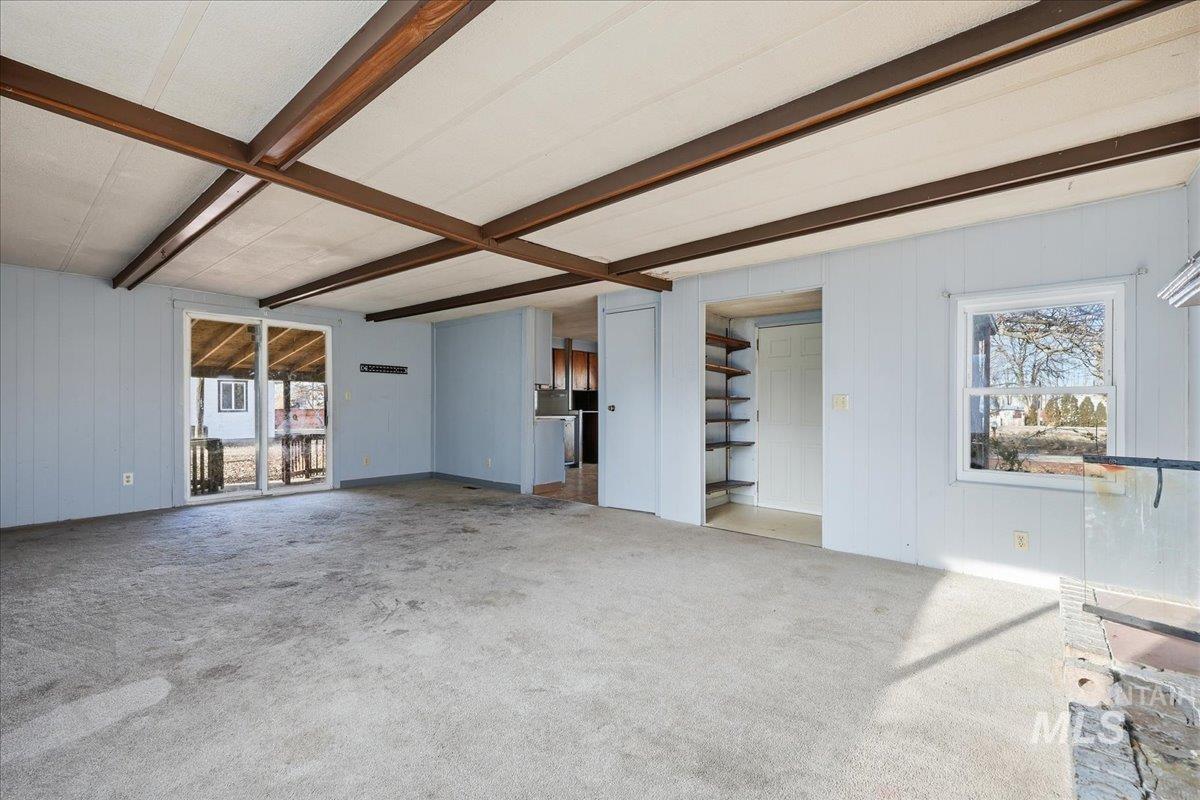 Unfurnished living room with wooden walls, beamed ceiling, plenty of natural light, carpet floors, and a decorative wall