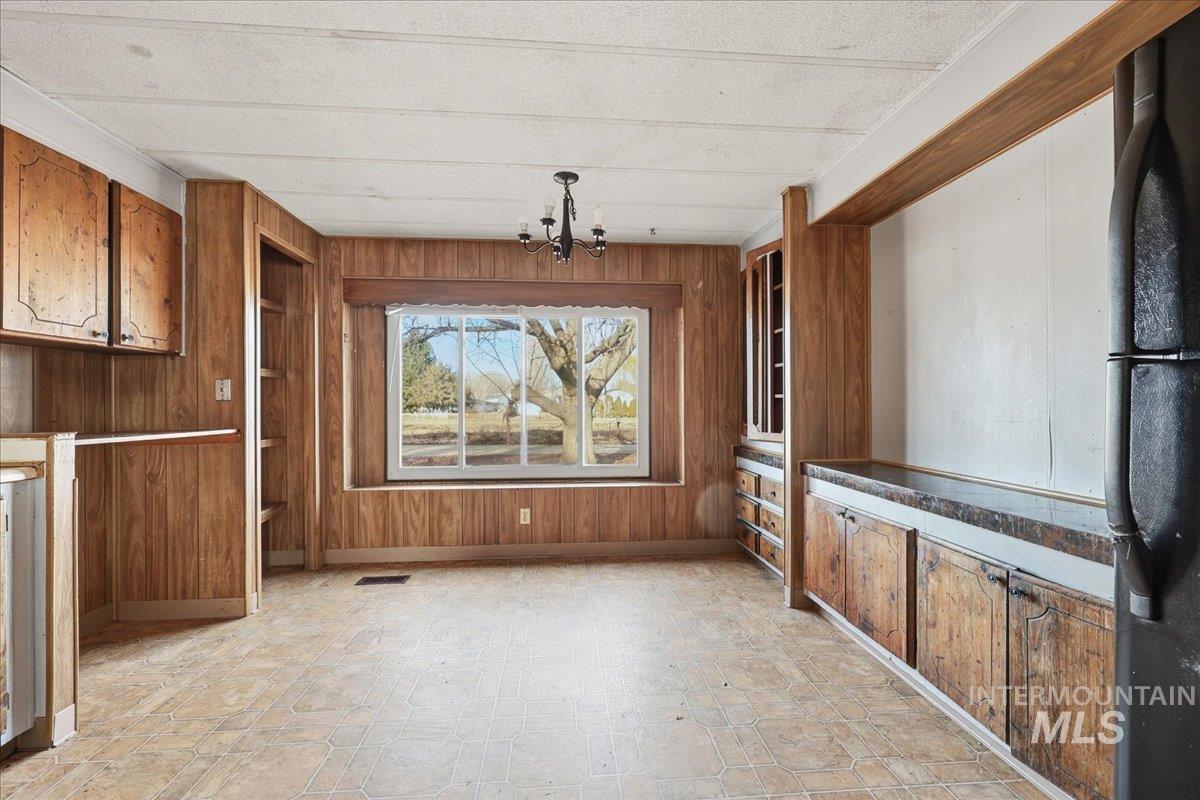 Unfurnished dining area featuring a chandelier, wooden walls, light flooring, and a textured ceiling