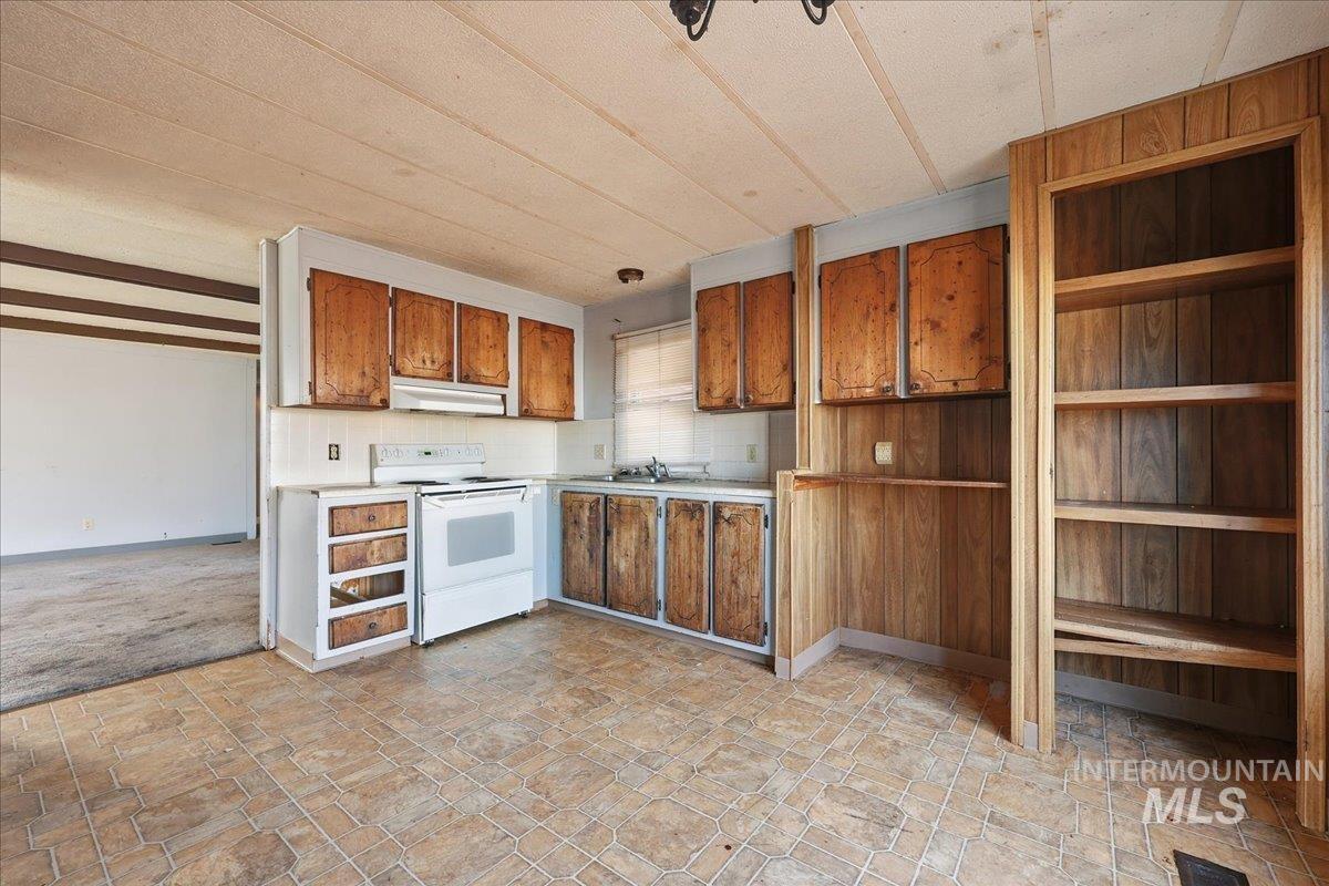 Kitchen with white range with electric stovetop, brown cabinetry, light countertops, under cabinet range hood, and open shelves