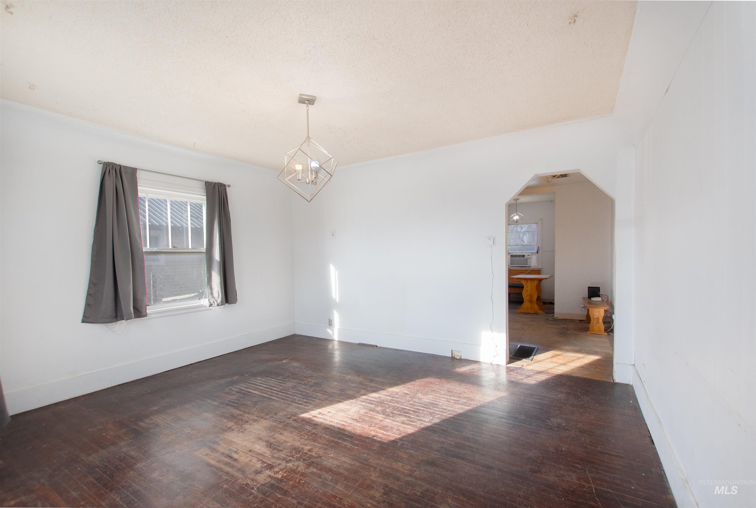 Empty room featuring dark wood finished floors, arched walkways, a chandelier, and a textured ceiling