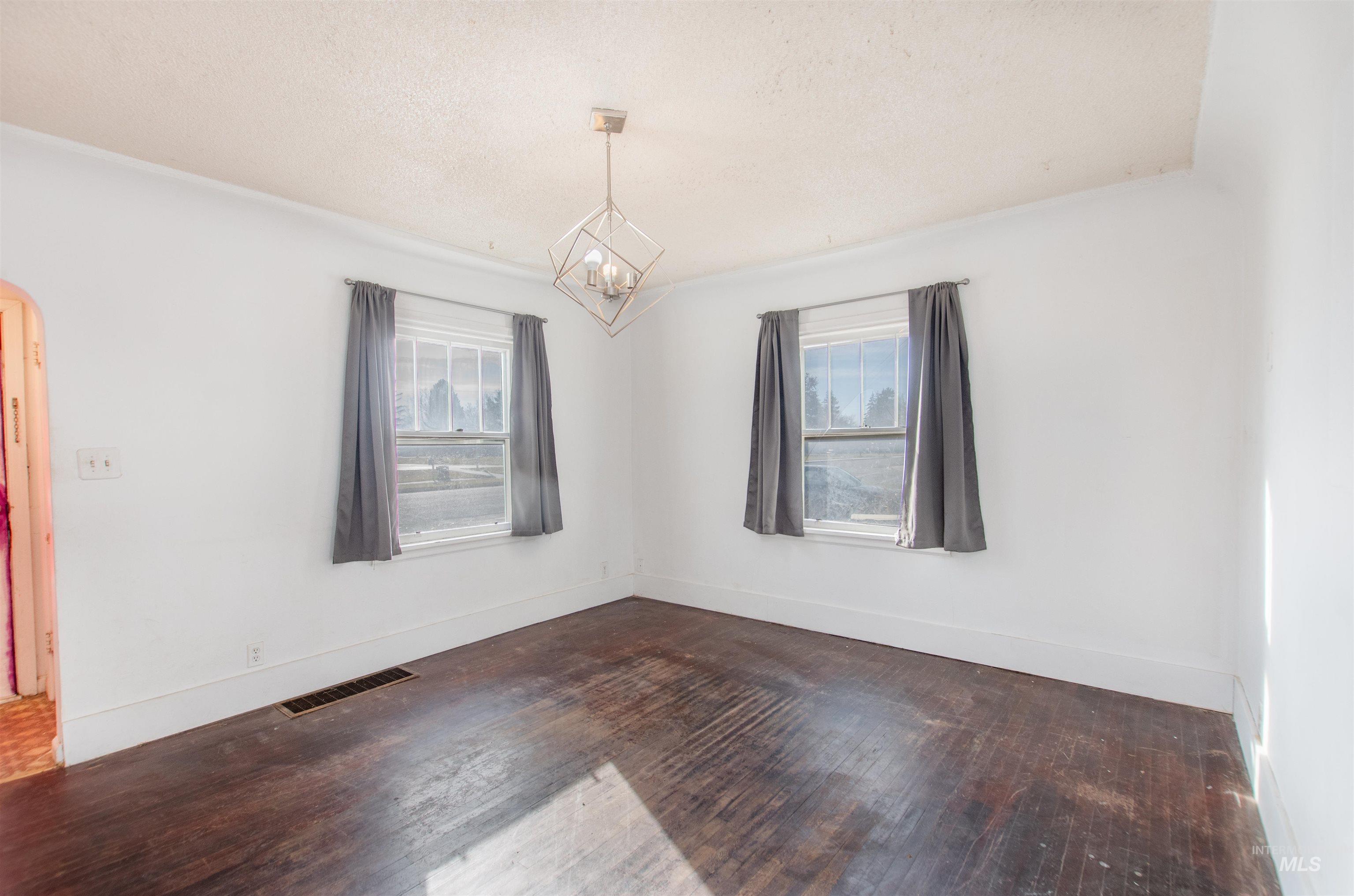 Unfurnished room with plenty of natural light, a textured ceiling, dark wood-type flooring, a chandelier, and arched walkways