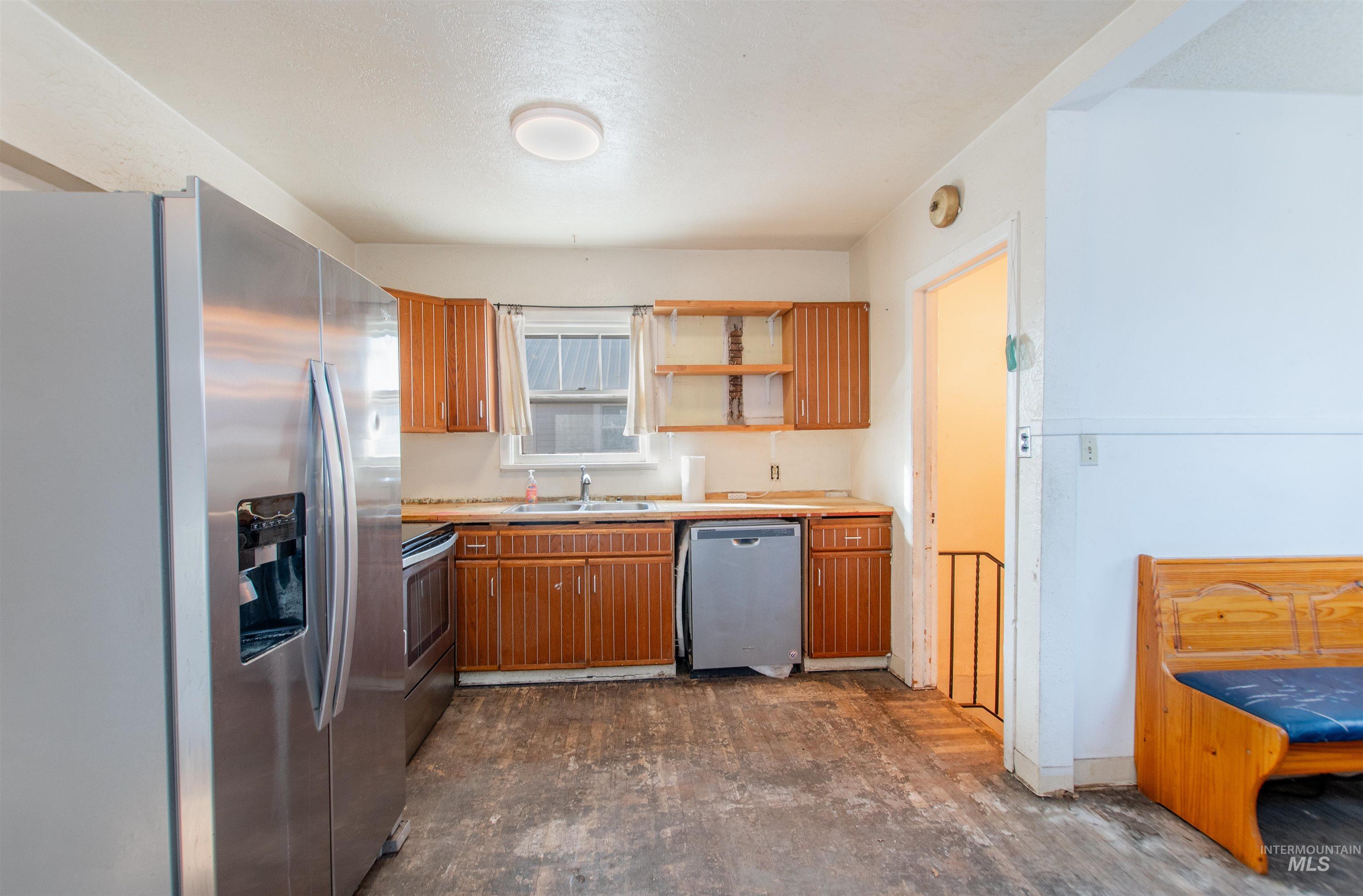 Kitchen featuring appliances with stainless steel finishes, light countertops, brown cabinetry, open shelves, and a textured ceiling