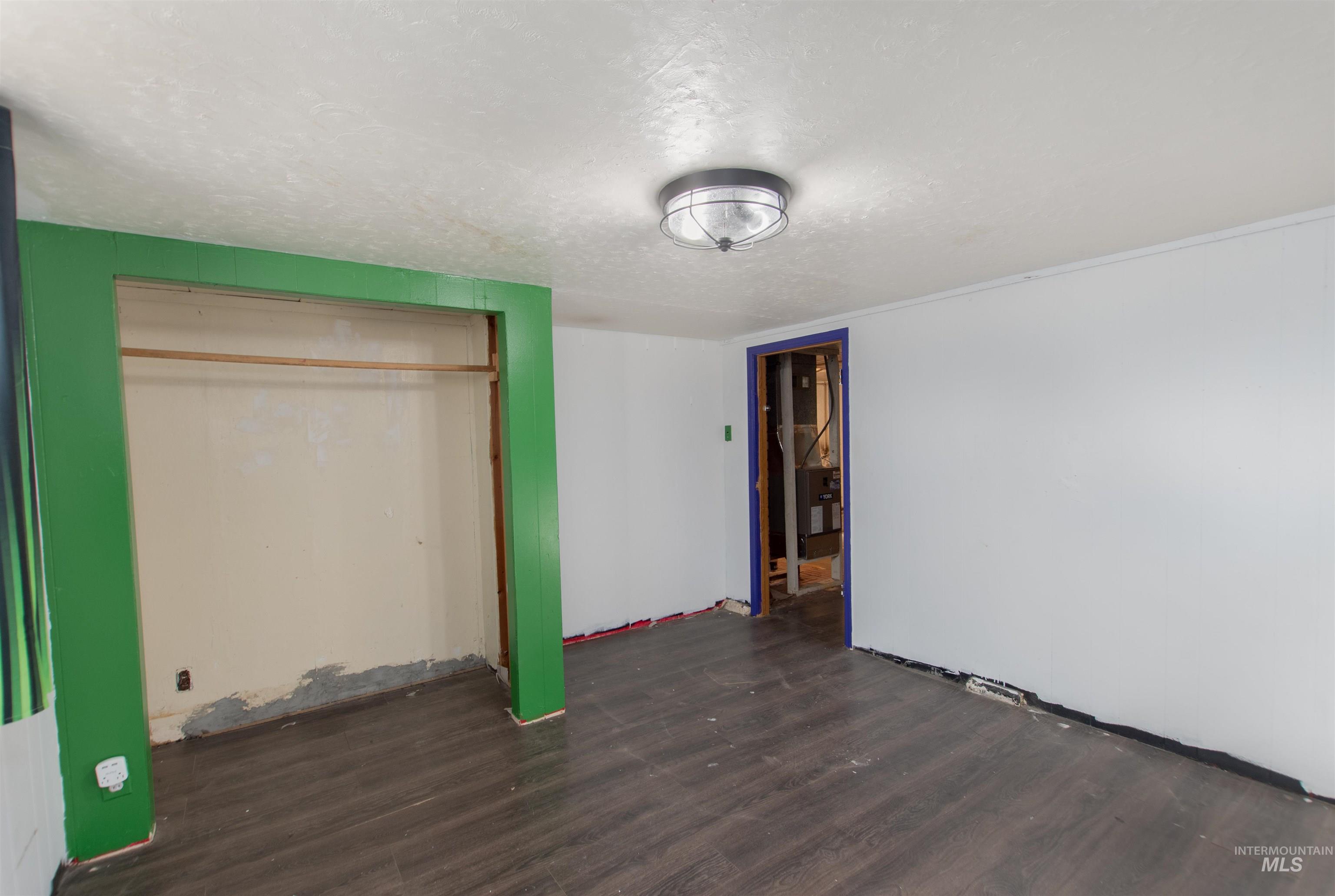 Unfurnished bedroom featuring a textured ceiling, dark wood-style floors, a closet, and heating unit