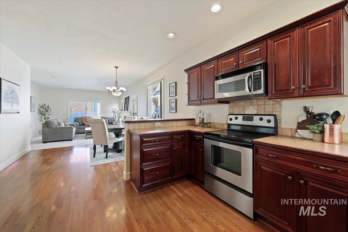 Kitchen with appliances with stainless steel finishes, decorative backsplash, open floor plan, pendant lighting, and a peninsula