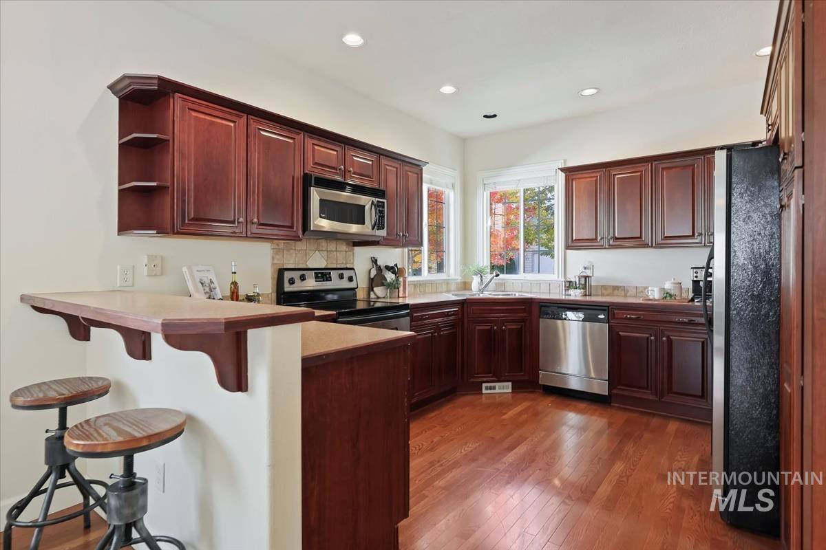 Kitchen with stainless steel appliances, open shelves, a peninsula, a kitchen bar, and dark wood finished floors