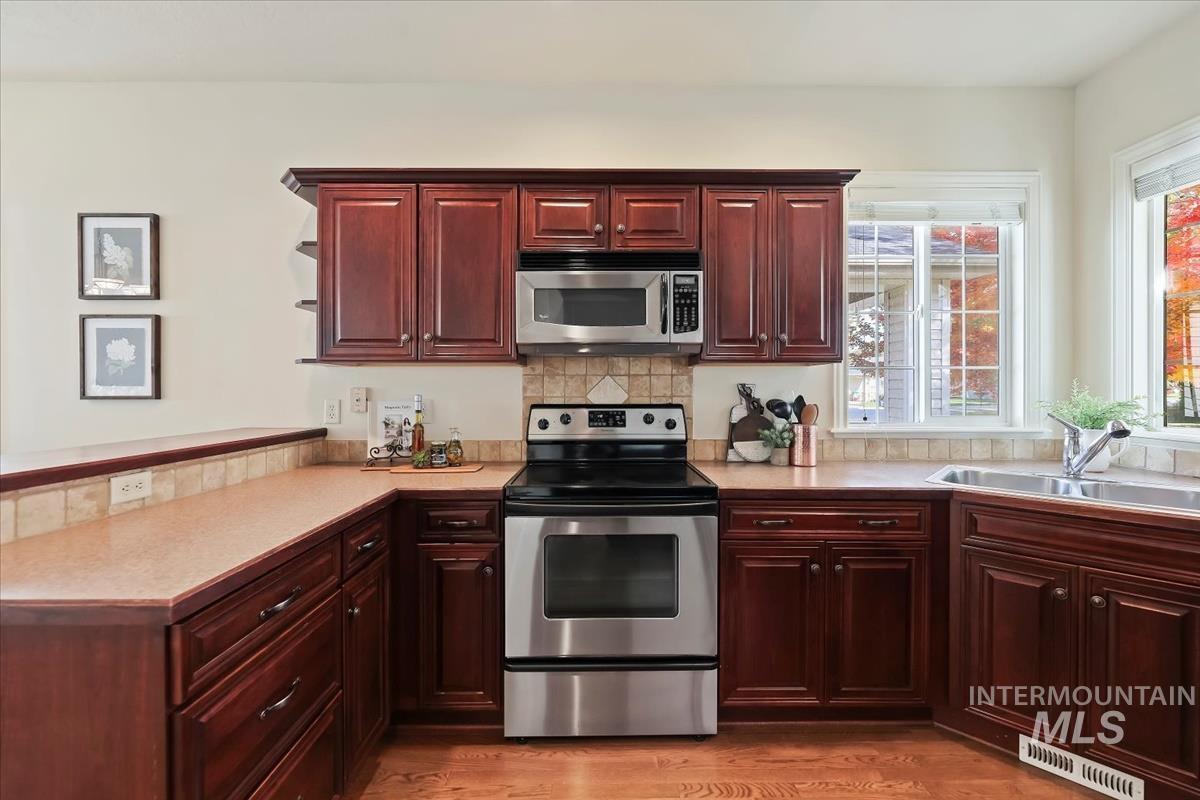 Kitchen featuring appliances with stainless steel finishes, reddish brown cabinets, backsplash, light countertops, and light wood finished floors