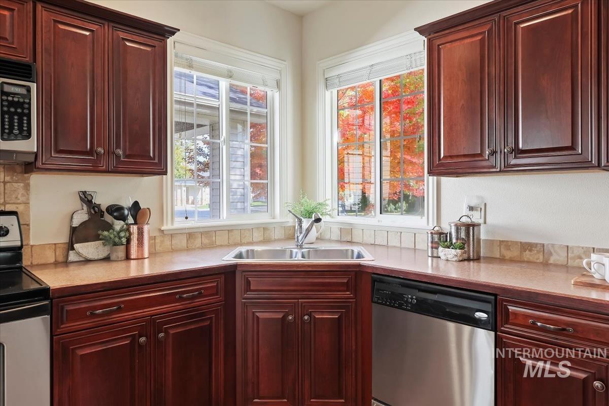 Kitchen with appliances with stainless steel finishes, light countertops, reddish brown cabinets, and healthy amount of natural light