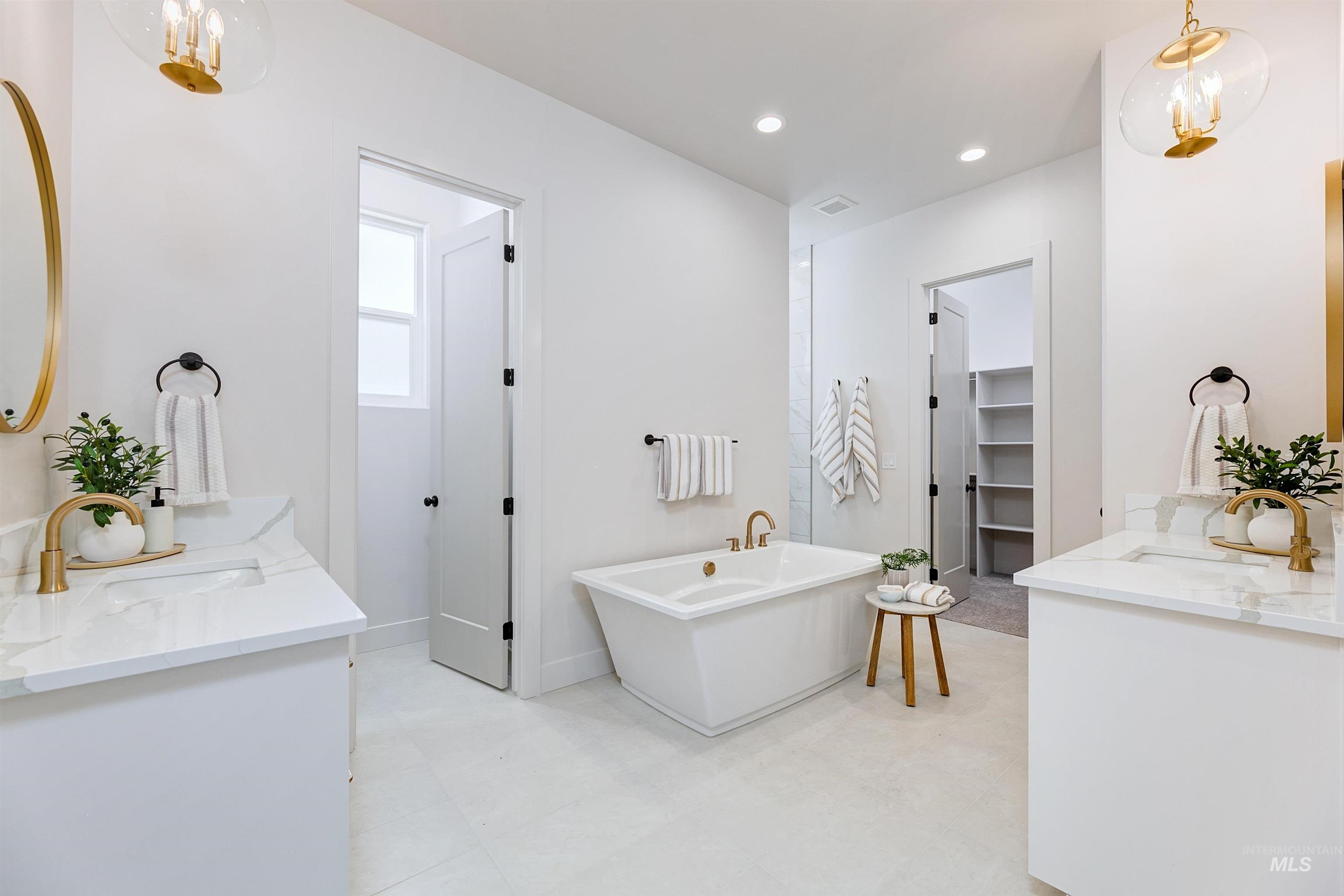 Bathroom featuring double vanity, a freestanding tub, a spacious closet, a chandelier, and recessed lighting