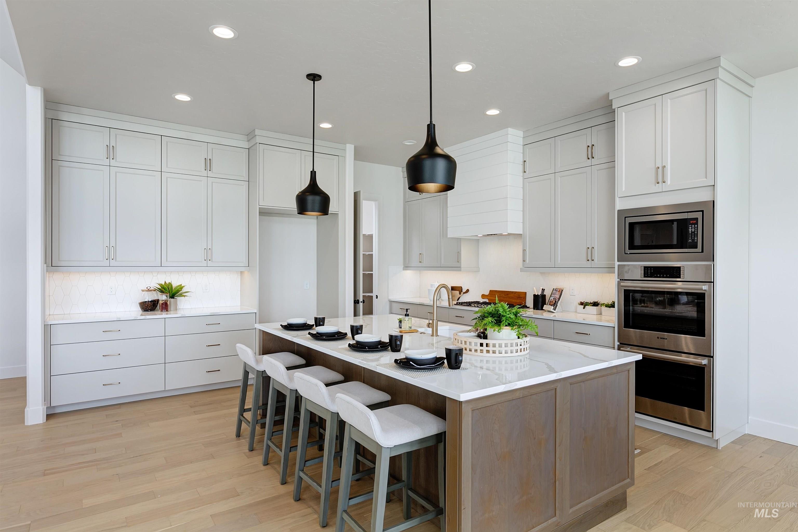 Kitchen featuring white cabinetry, hanging light fixtures, a breakfast bar area, a center island with sink, and stainless steel appliances
