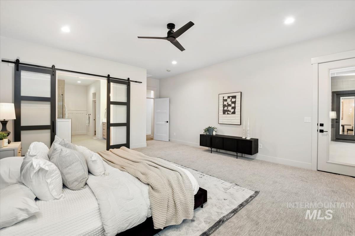 Bedroom featuring a barn door, carpet floors, a ceiling fan, and connected bathroom