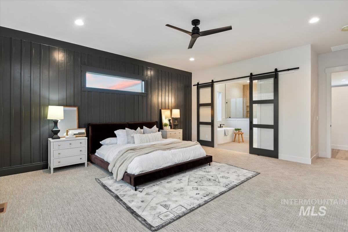 Bedroom with a barn door, light carpet, recessed lighting, a ceiling fan, and ensuite bathroom