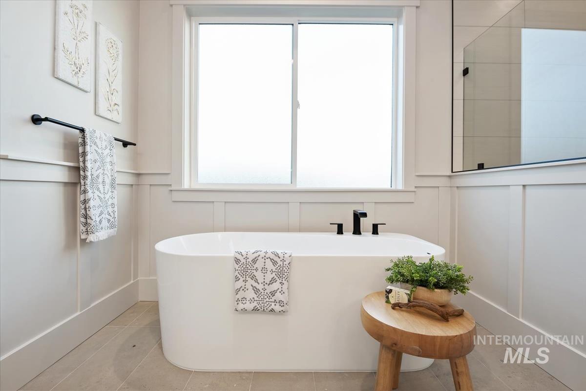 Full bathroom with a decorative wall, a freestanding tub, healthy amount of natural light, wainscoting, and light tile patterned floors