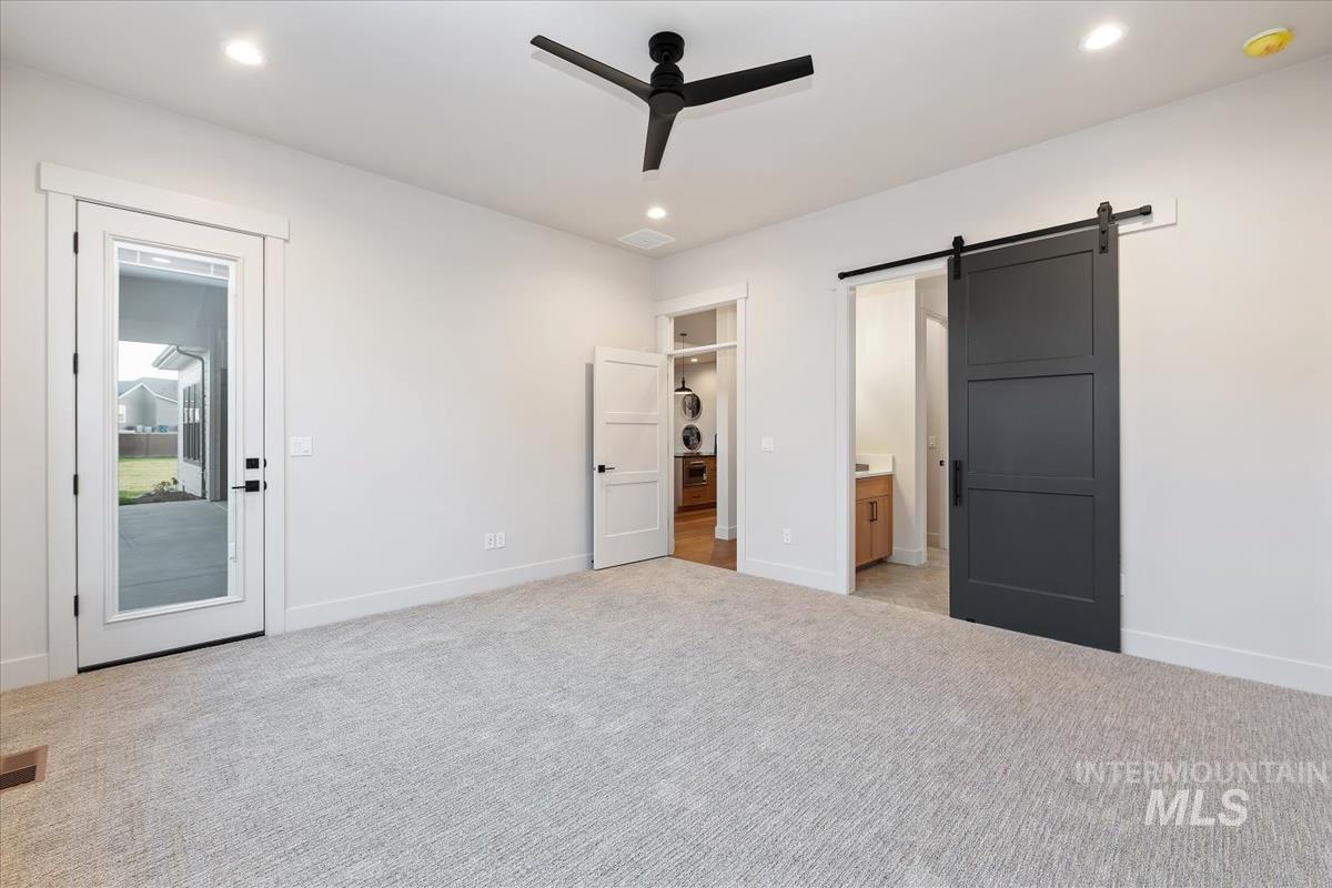Unfurnished bedroom featuring a barn door, light colored carpet, ceiling fan, access to outside, and connected bathroom
