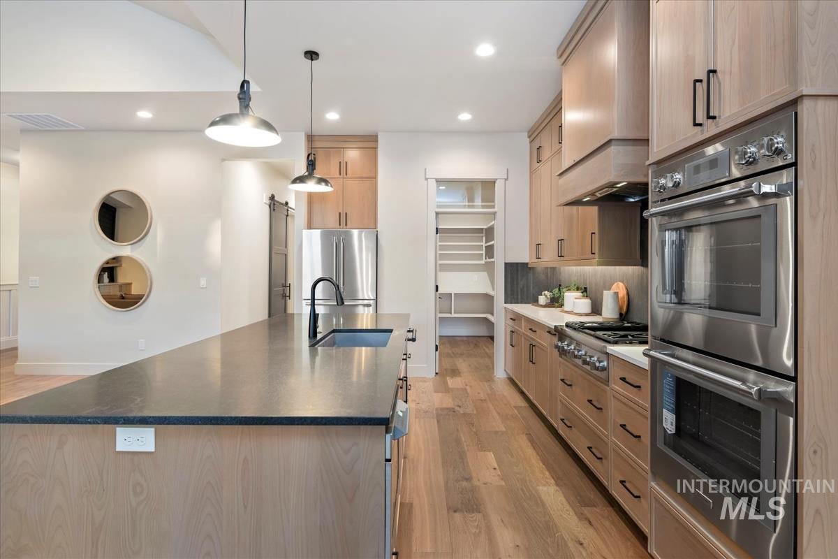 Kitchen with light brown cabinets, appliances with stainless steel finishes, light wood finished floors, a spacious island, and hanging light fixtures