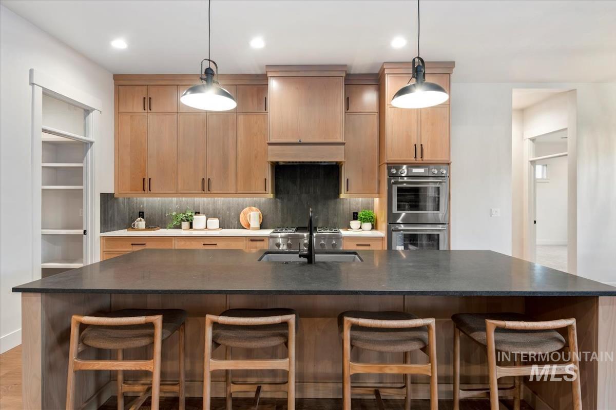 Kitchen featuring backsplash, stainless steel double oven, dark stone counters, and decorative light fixtures