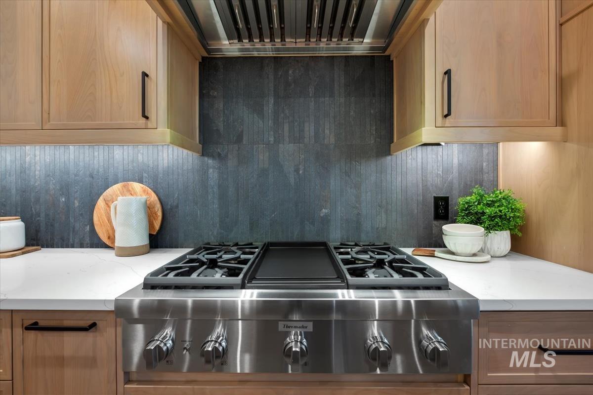 Kitchen featuring stainless steel gas cooktop, light stone counters, custom exhaust hood, and tasteful backsplash