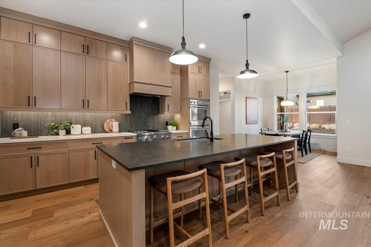 Kitchen with light brown cabinetry, hanging light fixtures, a center island with sink, decorative backsplash, and a breakfast bar