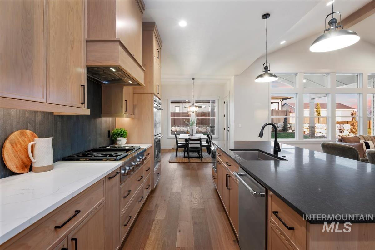 Kitchen featuring dark stone counters, hanging light fixtures, dark wood-type flooring, appliances with stainless steel finishes, and vaulted ceiling